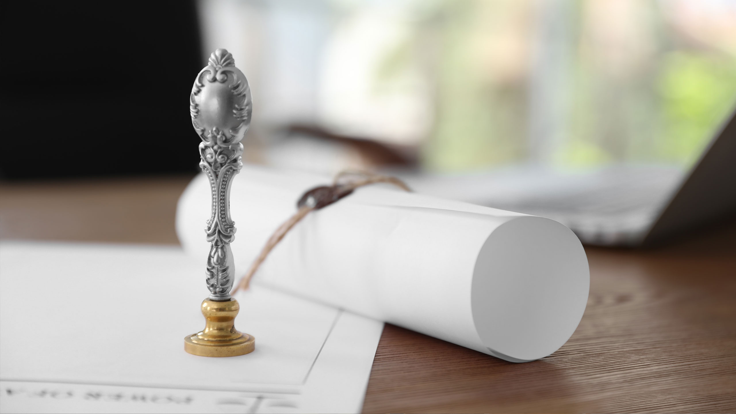 Close-up of a document seal stamp beside rolled property documents on a desk with a laptop in the background