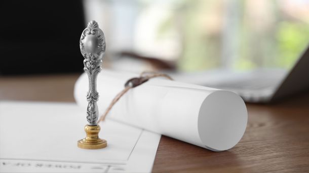 Close-up of a document seal stamp beside rolled property documents on a desk with a laptop in the background